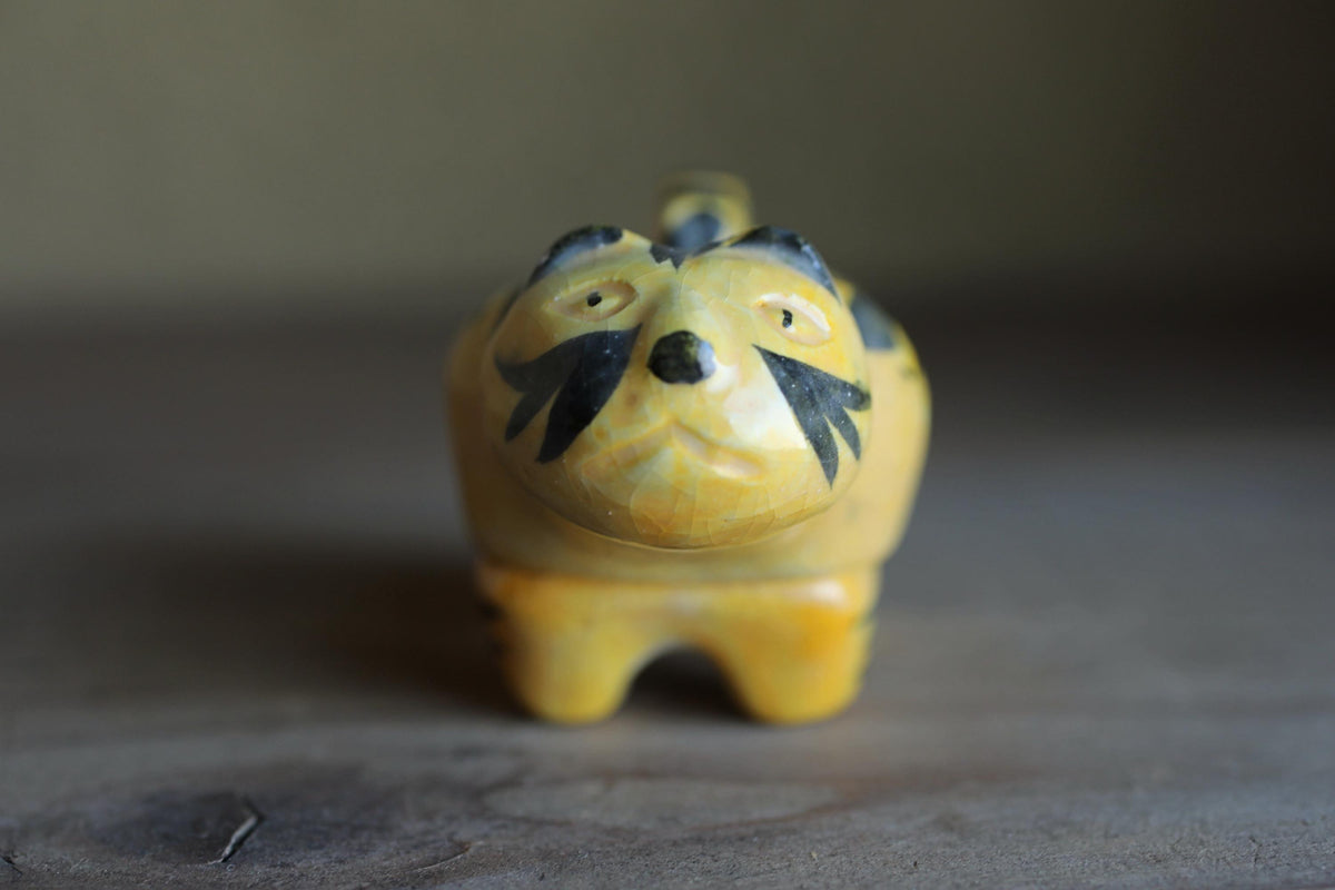 A small yellow and black figurine of a cat is sitting on a wooden surface.