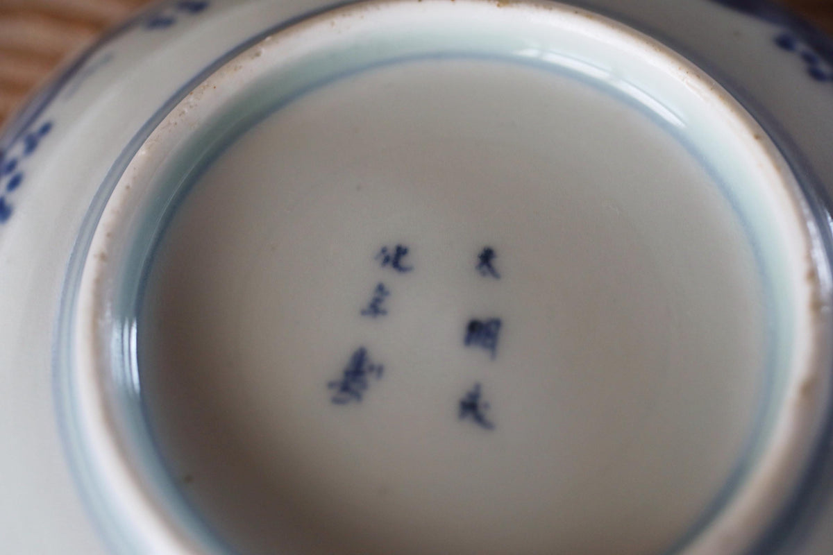 A close-up view of a white ceramic plate with blue designs and Chinese characters.