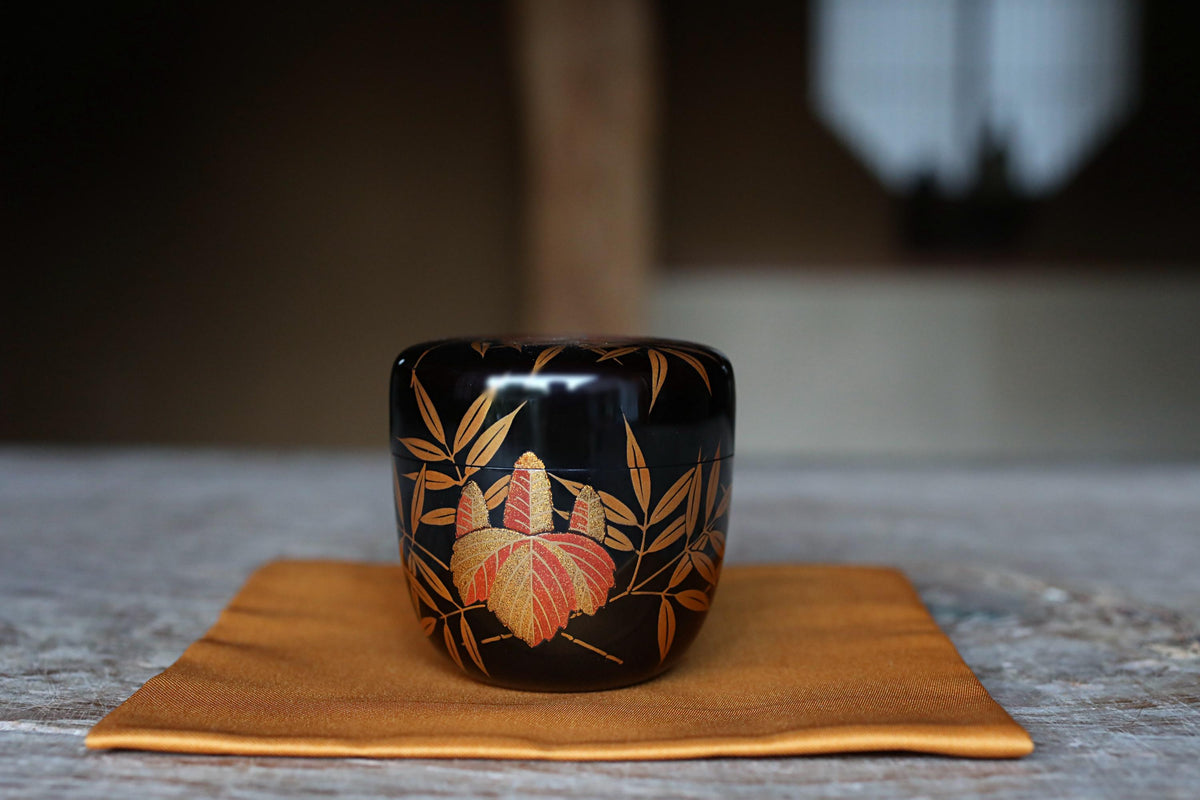 A black ceramic container with a floral design sits on a brown cloth on a wooden surface.