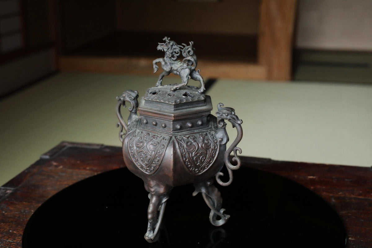 A decorative metal incense burner with an ornate lid featuring a dragon and other mythical creatures.