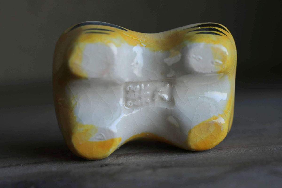 A ceramic figurine with a yellow and white color scheme, featuring a distinctive design on its surface.