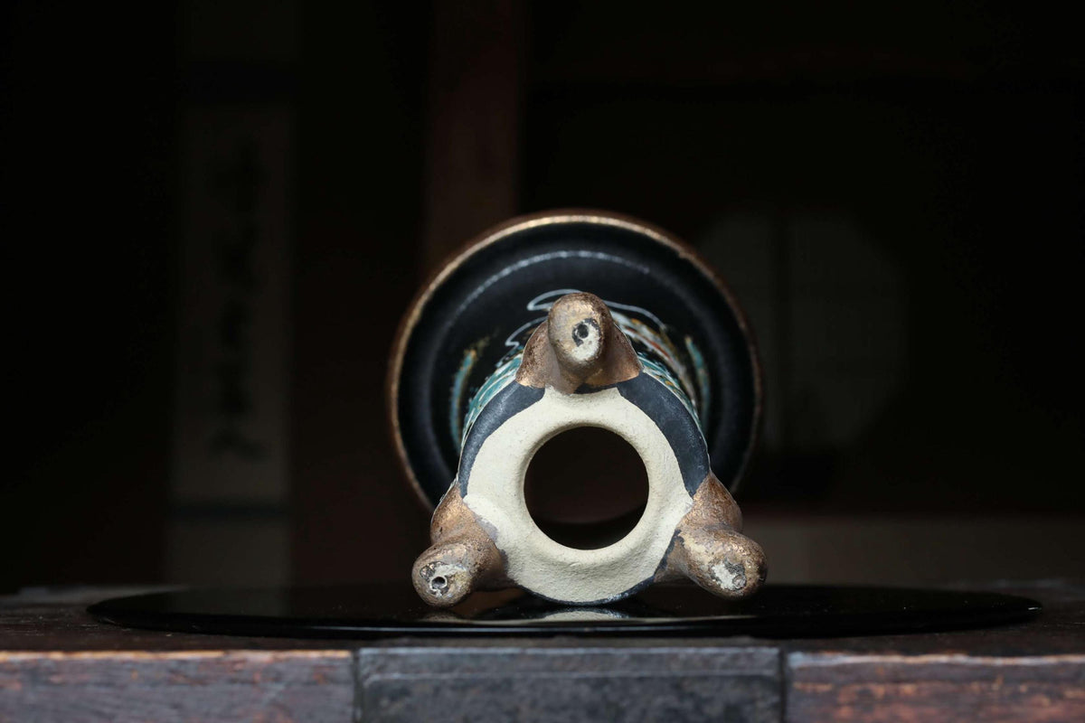 A ceramic vase with a black base and a white interior sits on a wooden surface, its intricate design and craftsmanship visible.