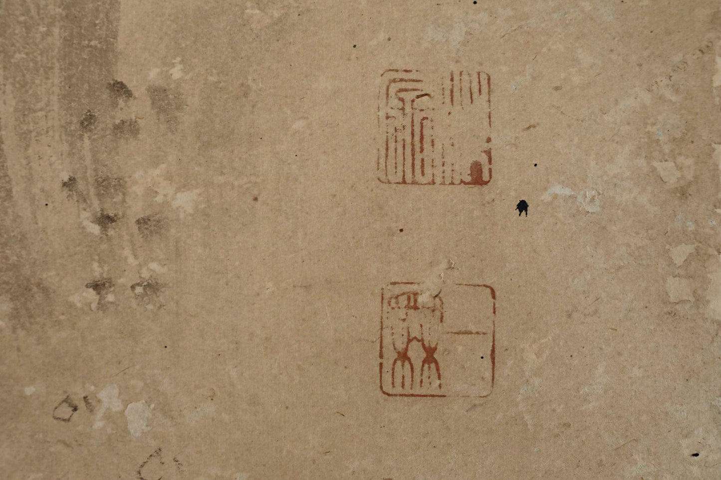 a textured surface with two distinct symbols or designs, one larger and one smaller, both in red color. There is also a small black dot or line near the larger symbol.