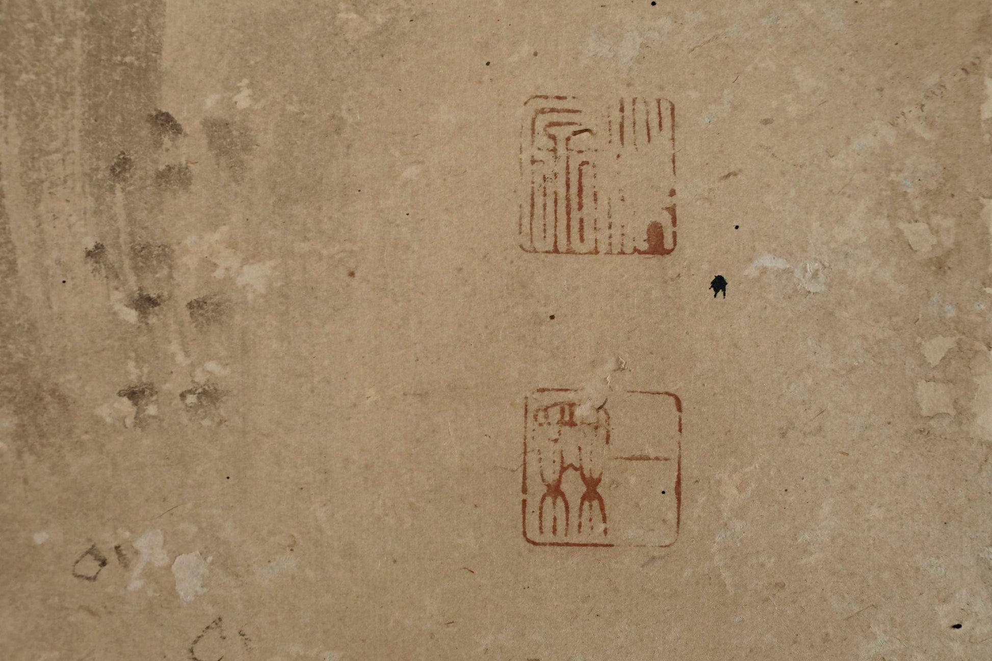 a textured surface with two distinct symbols or designs, one larger and one smaller, both in red color. There is also a small black dot or line near the larger symbol.