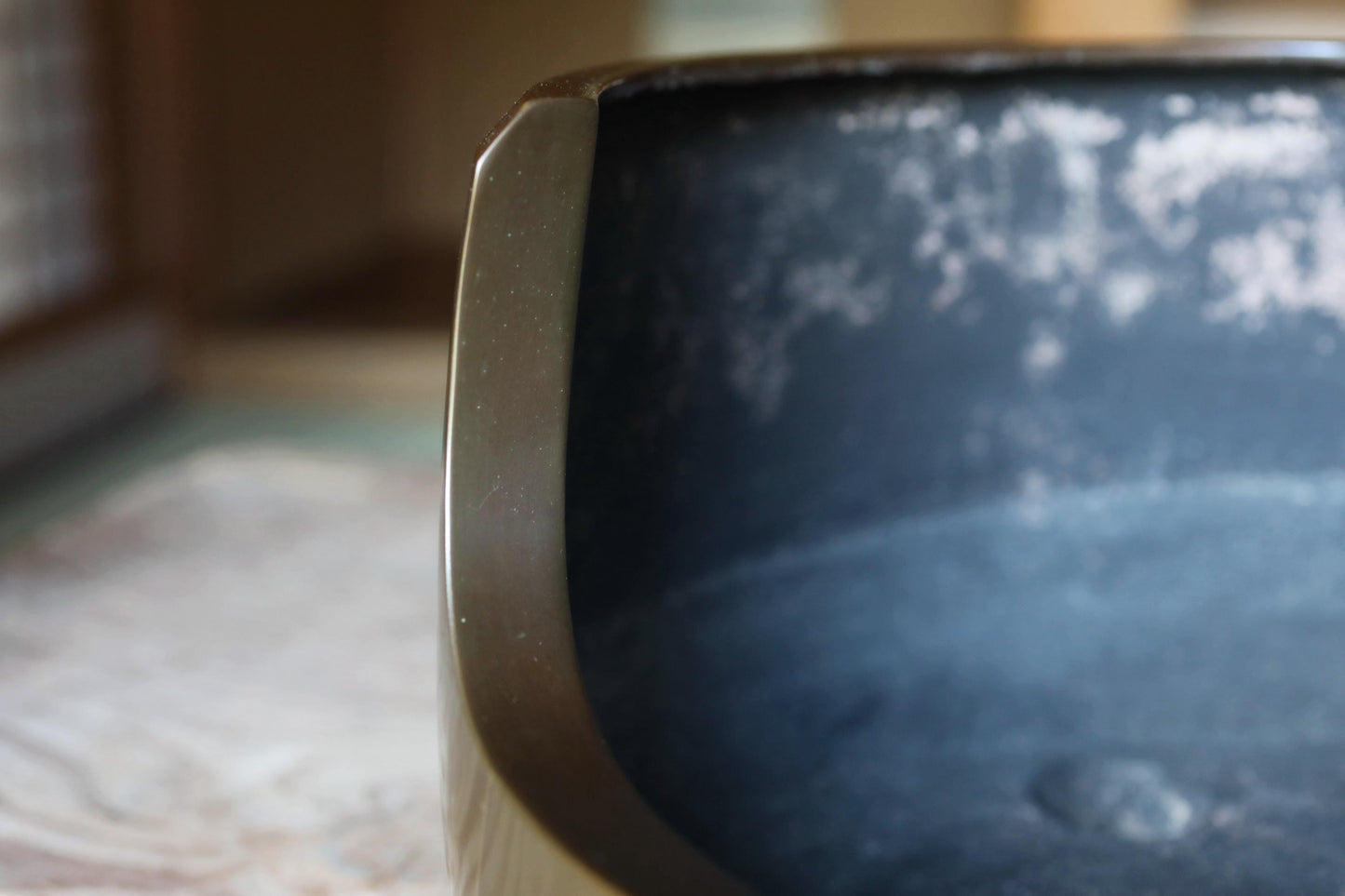 A close-up view of a metal container with a dark, textured surface, possibly a pot or vase, with a blurred background.