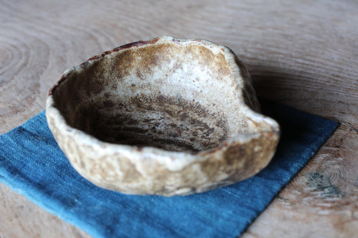 A ceramic bowl with a textured surface sits on a blue cloth on a wooden surface.