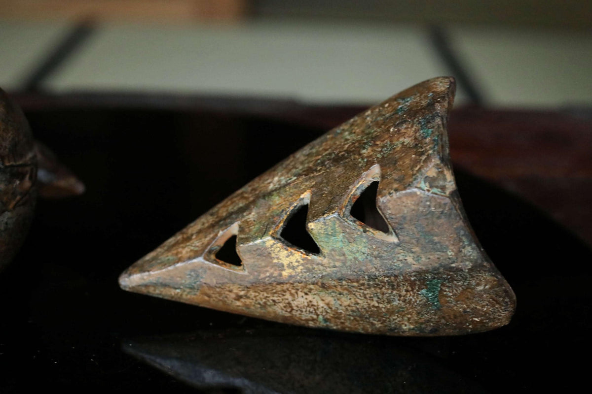 a close-up view of a weathered, rusted metal object with a triangular shape and a hole in the center.