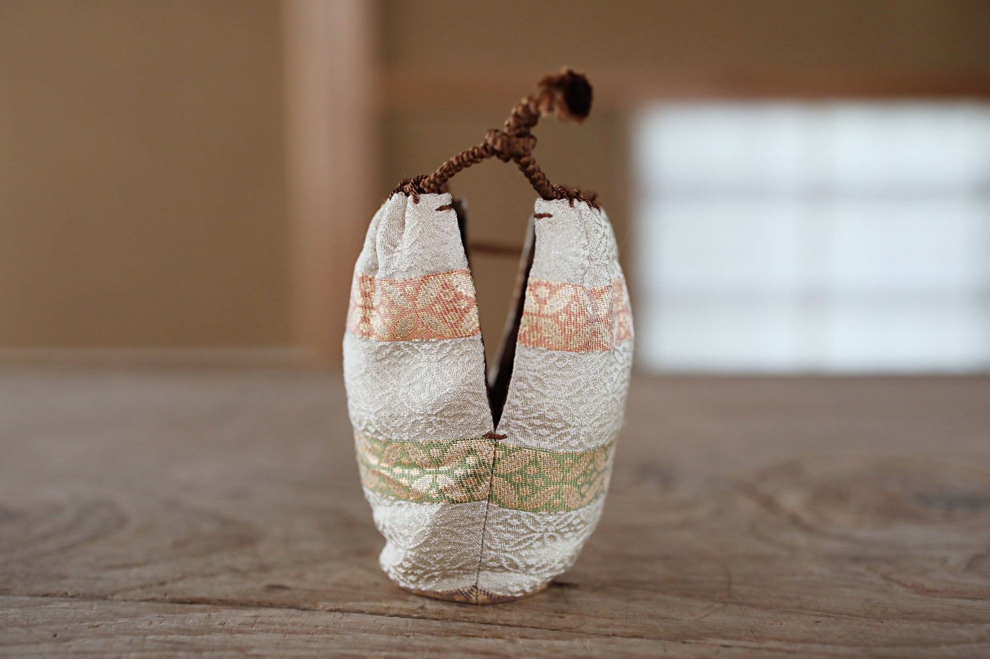 A small, white, fabric bag with a floral pattern sits on a wooden surface.