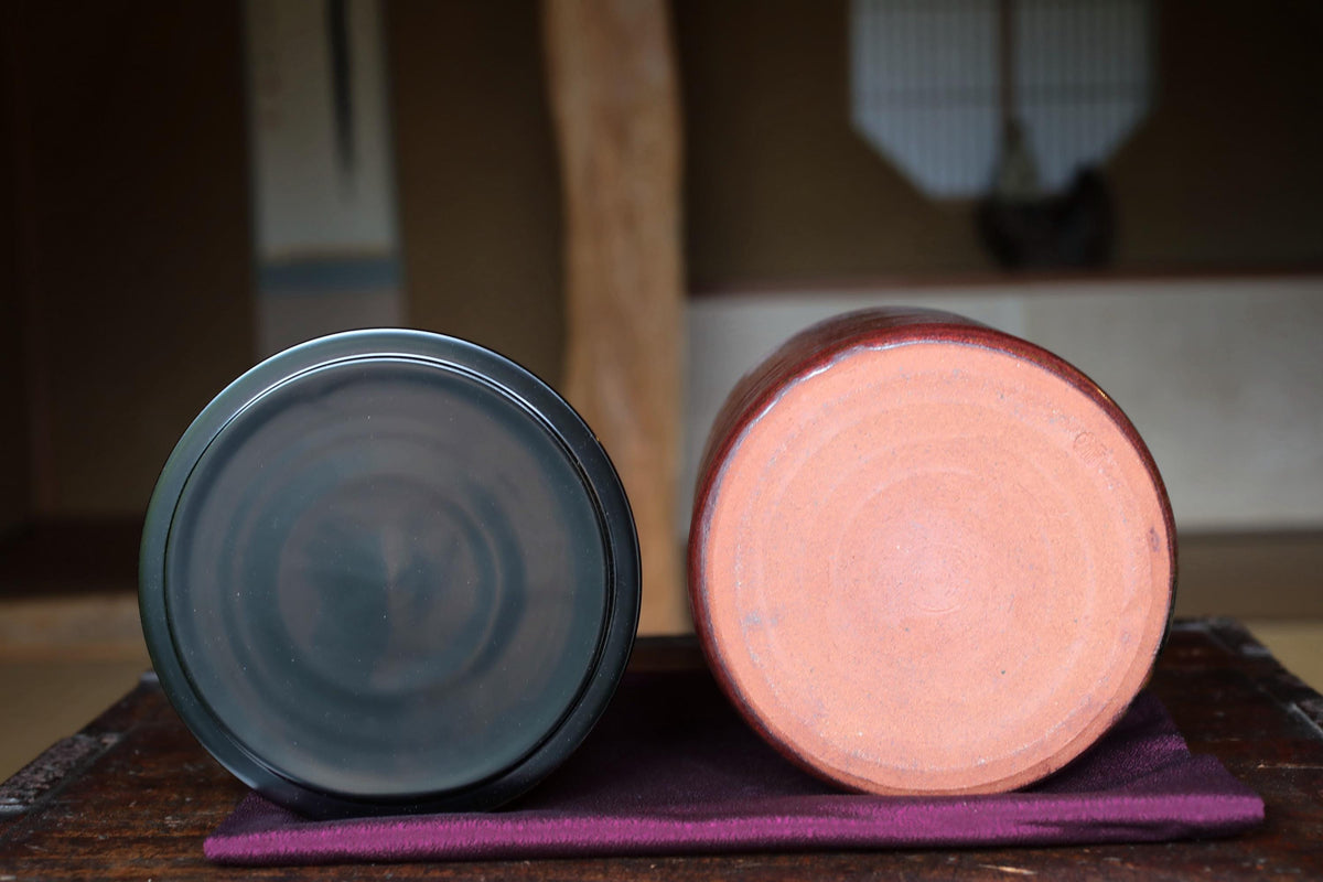 Two ceramic vases, one black and one red, are placed side by side on a wooden surface.