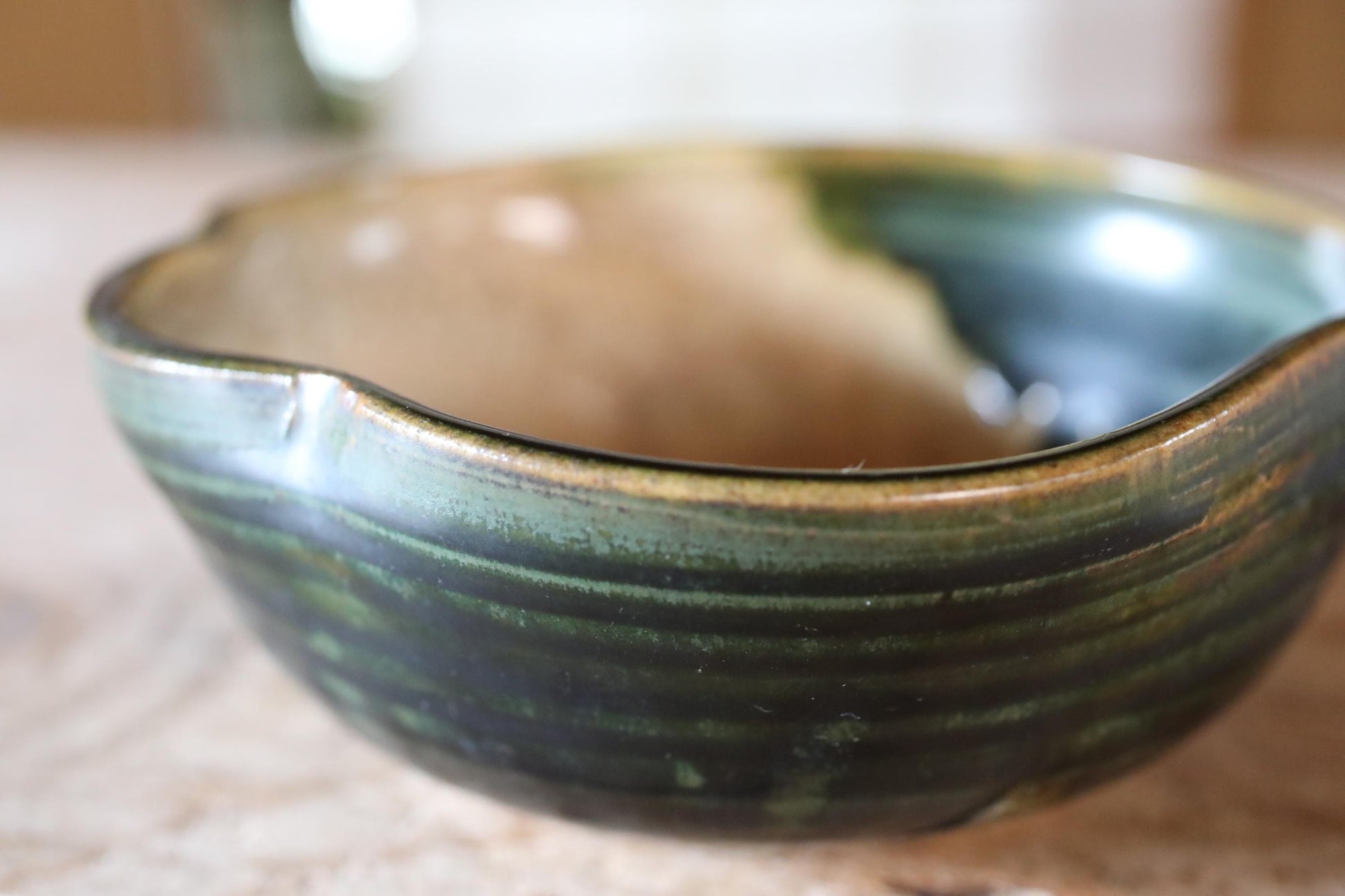 A close-up image of a ceramic bowl with a green and brown color scheme, sitting on a surface.