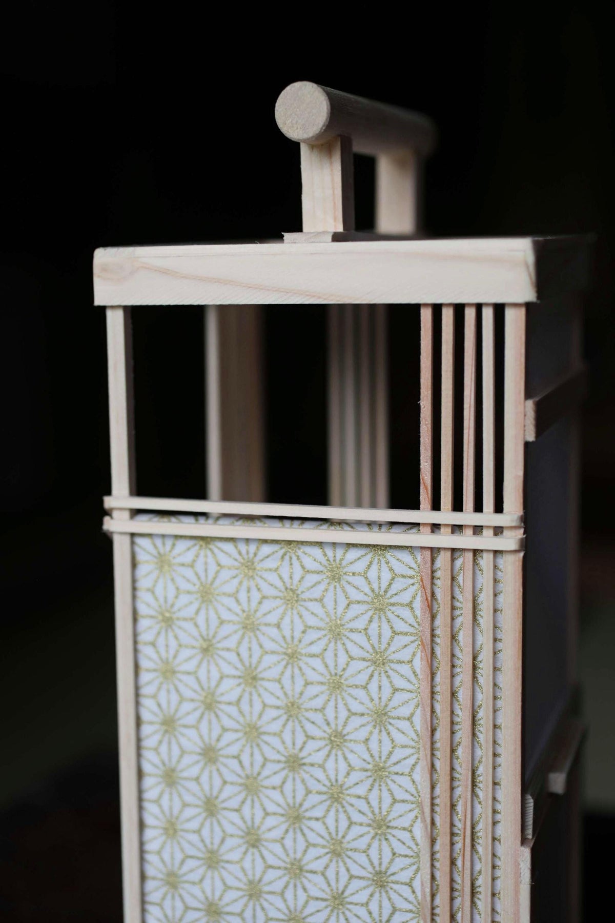 A wooden lantern with a geometric patterned paper covering, featuring a wooden handle on top.