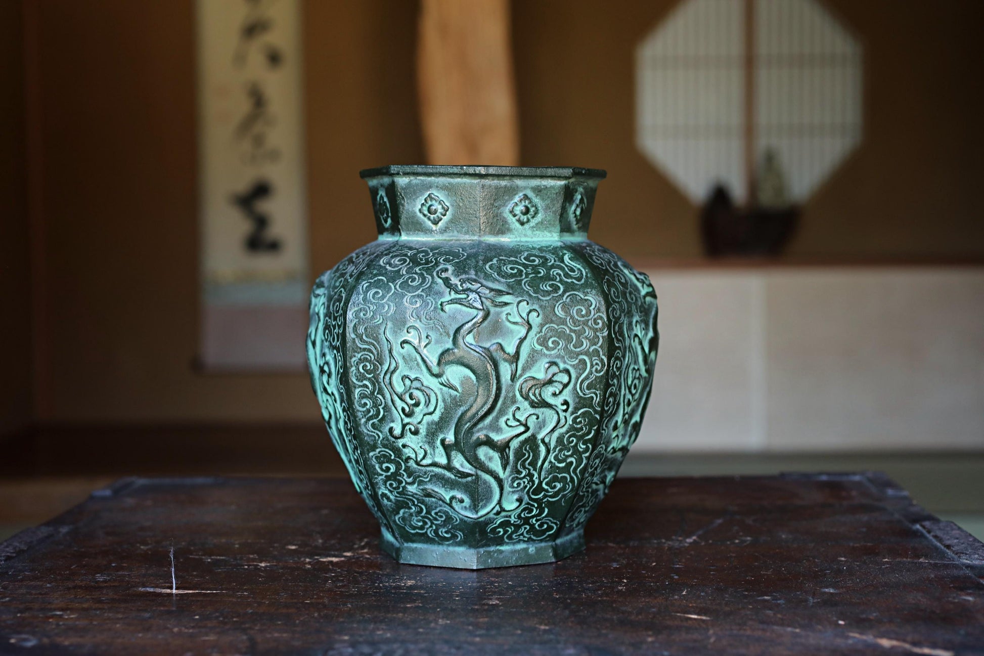 A decorative green vase with intricate designs sits on a wooden surface.