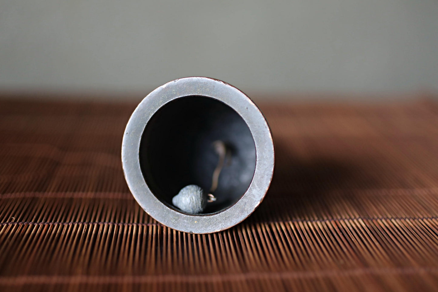 A ceramic bell with a small object inside rests on a woven surface.