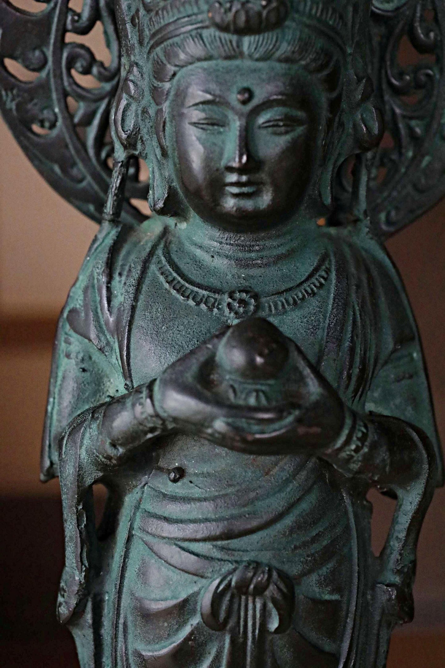 A bronze statue of a deity holding a ball, with intricate details and a serene expression.