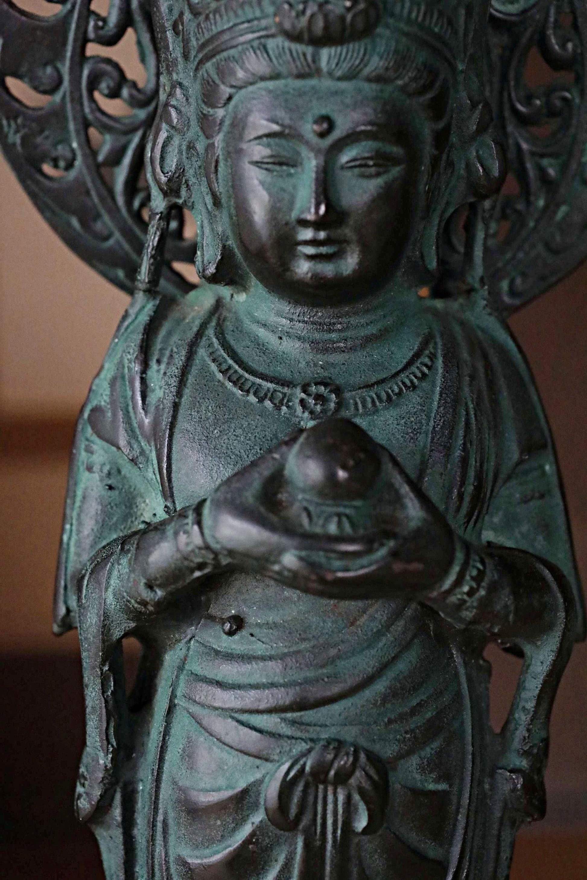 A bronze statue of a deity holding a ball, with intricate details and a serene expression.