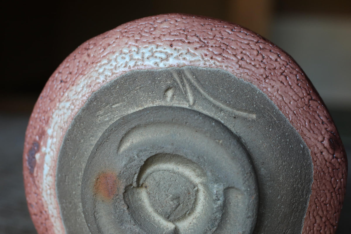 A close-up image of a ceramic object with a textured surface, featuring a circular pattern and a small hole in the center.
