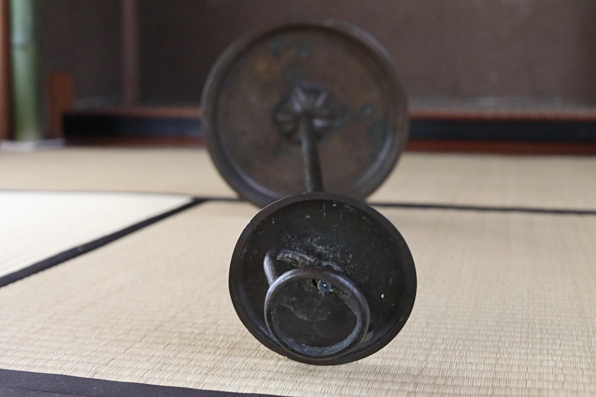 a close-up view of a metal object, possibly a candle holder or a small sculpture, resting on a woven mat or mat-like surface.