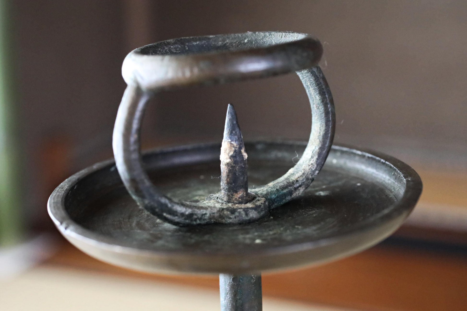 A close-up view of an old, rusted metal candle holder with a small, sharp object protruding from it.