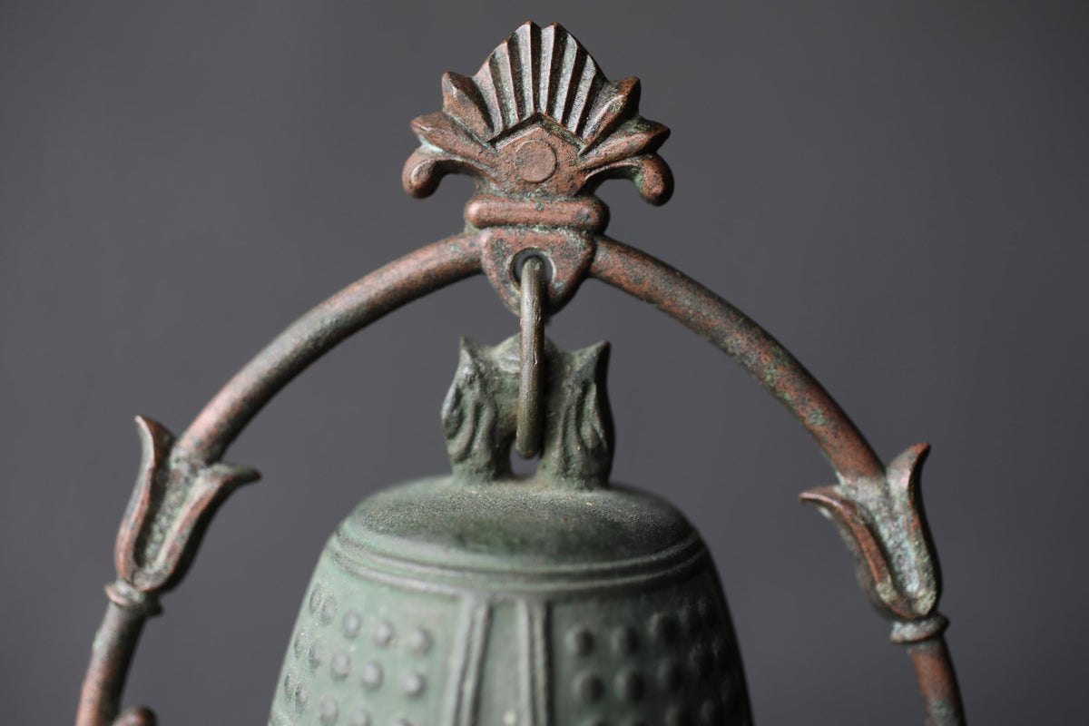 A close-up view of a decorative metal bell with an ornate, floral-inspired design on top.
