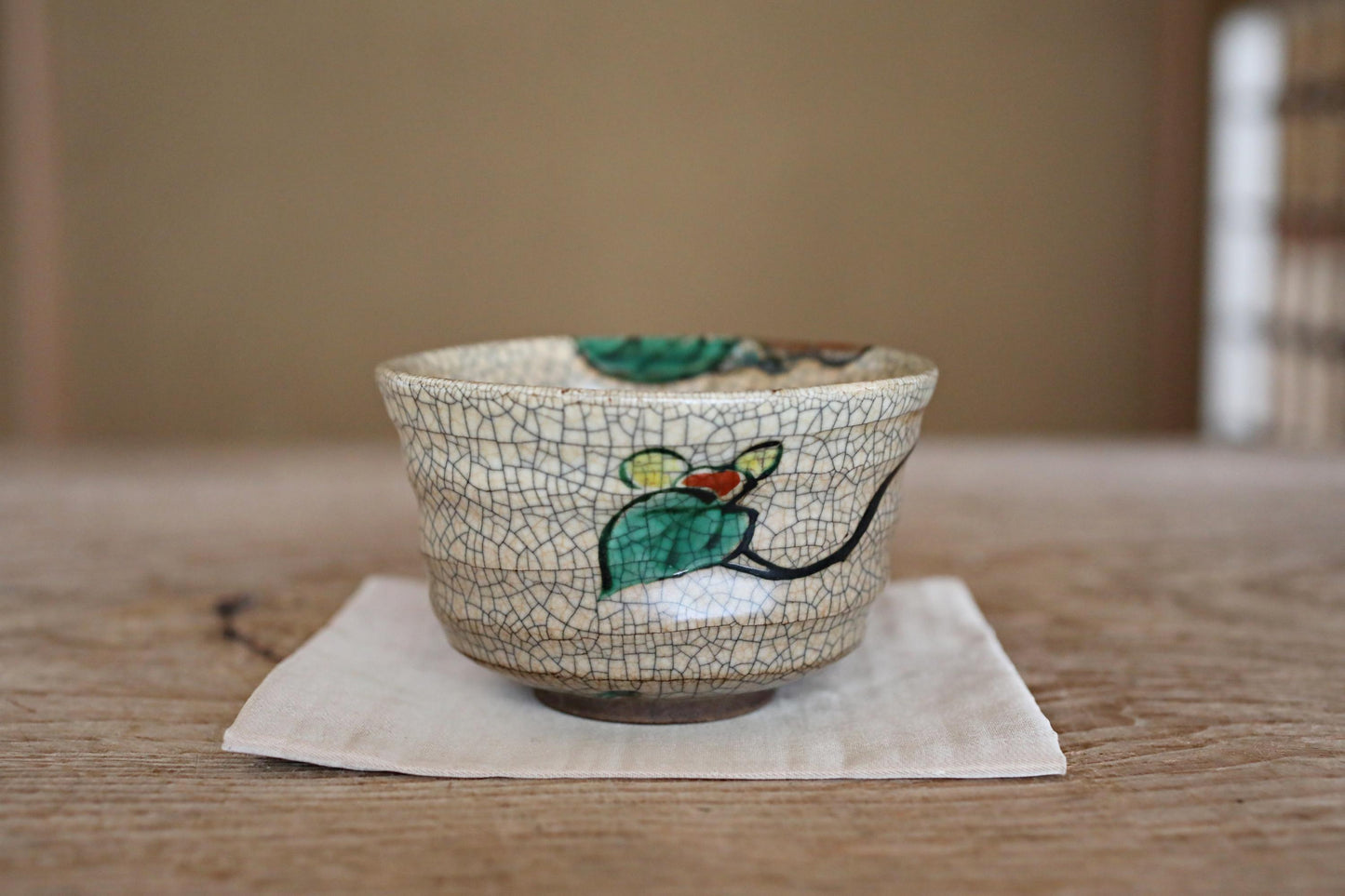 A ceramic bowl with a green leaf design sits on a white napkin on a wooden table.
