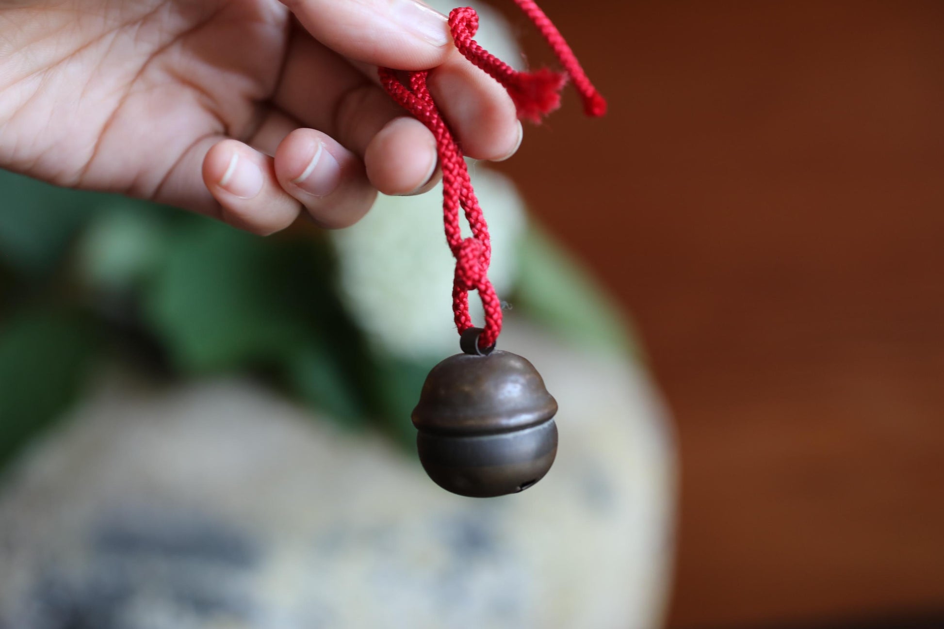 A hand holding a red string with a small, round bell attached to it.