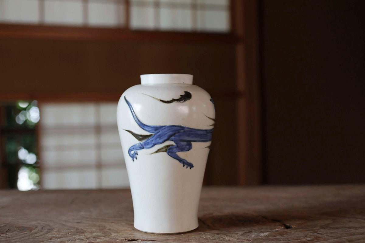 A white ceramic vase with a blue dragon design on it, placed on a wooden surface.