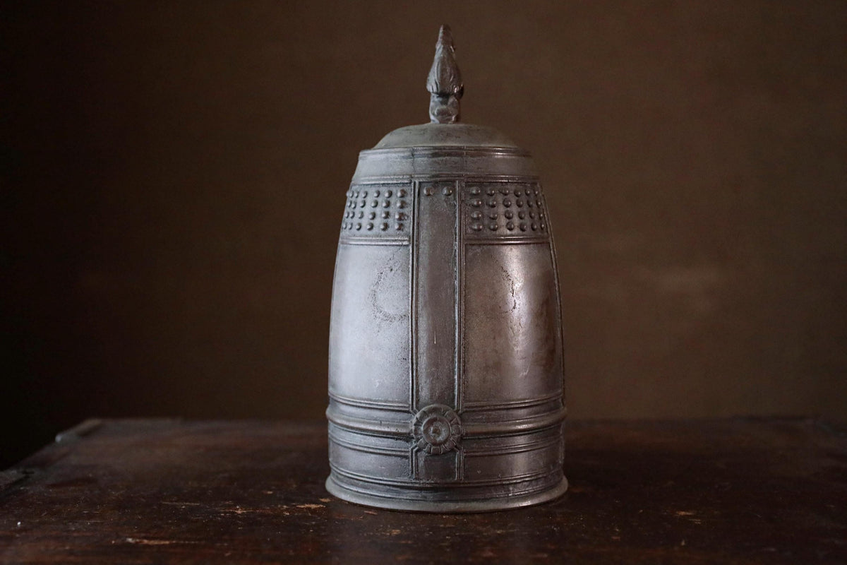 A metal container with a decorative top sits on a wooden surface against a dark background.