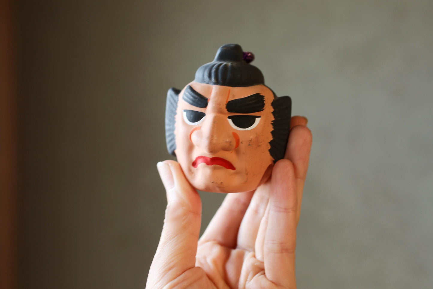 A hand holding a toy resembling a Japanese warrior or samurais head.