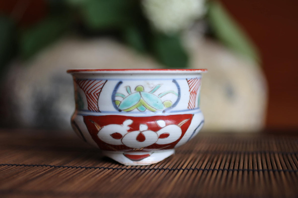 A colorful ceramic bowl with a red rim and intricate designs sits on a bamboo mat.