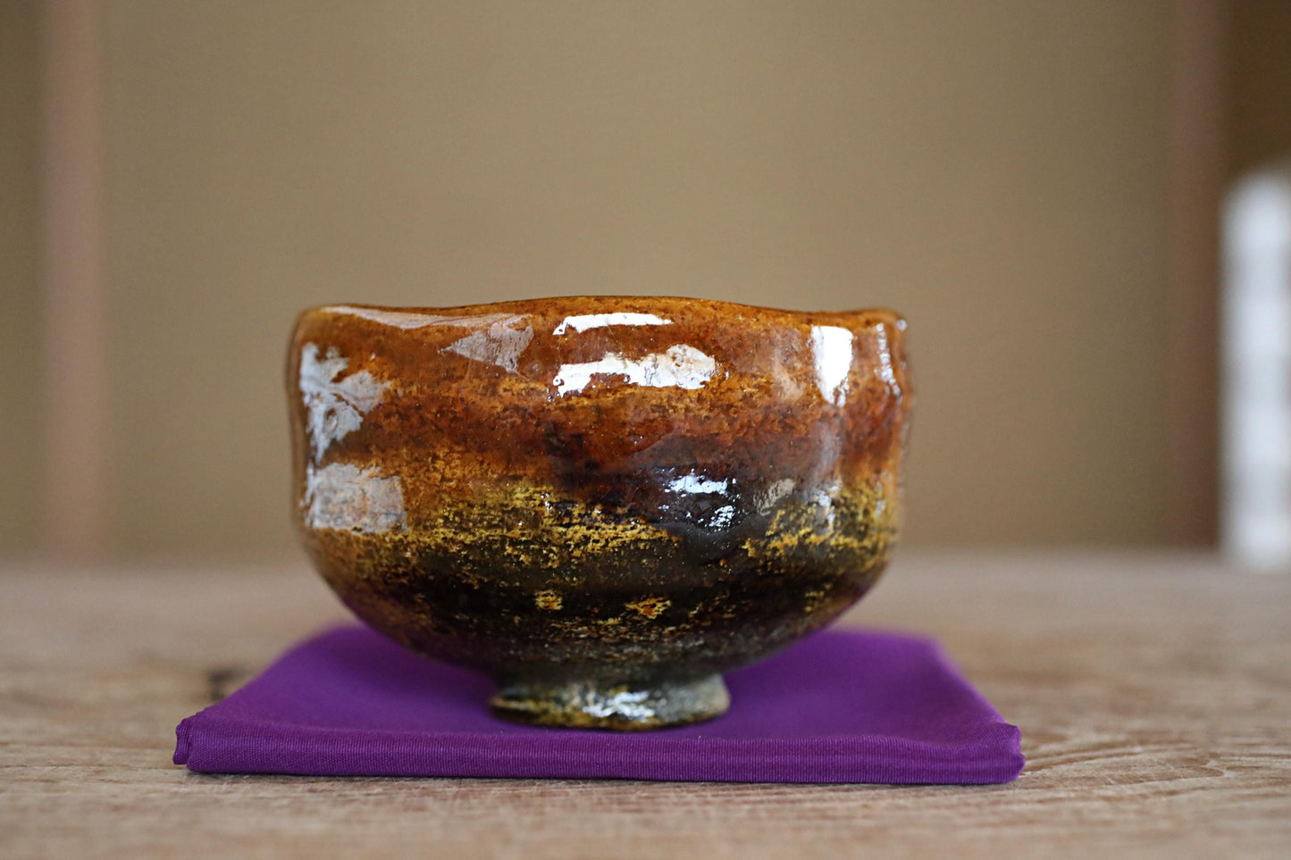 A ceramic bowl with a brown and orange color scheme sits on a purple cloth on a wooden surface.