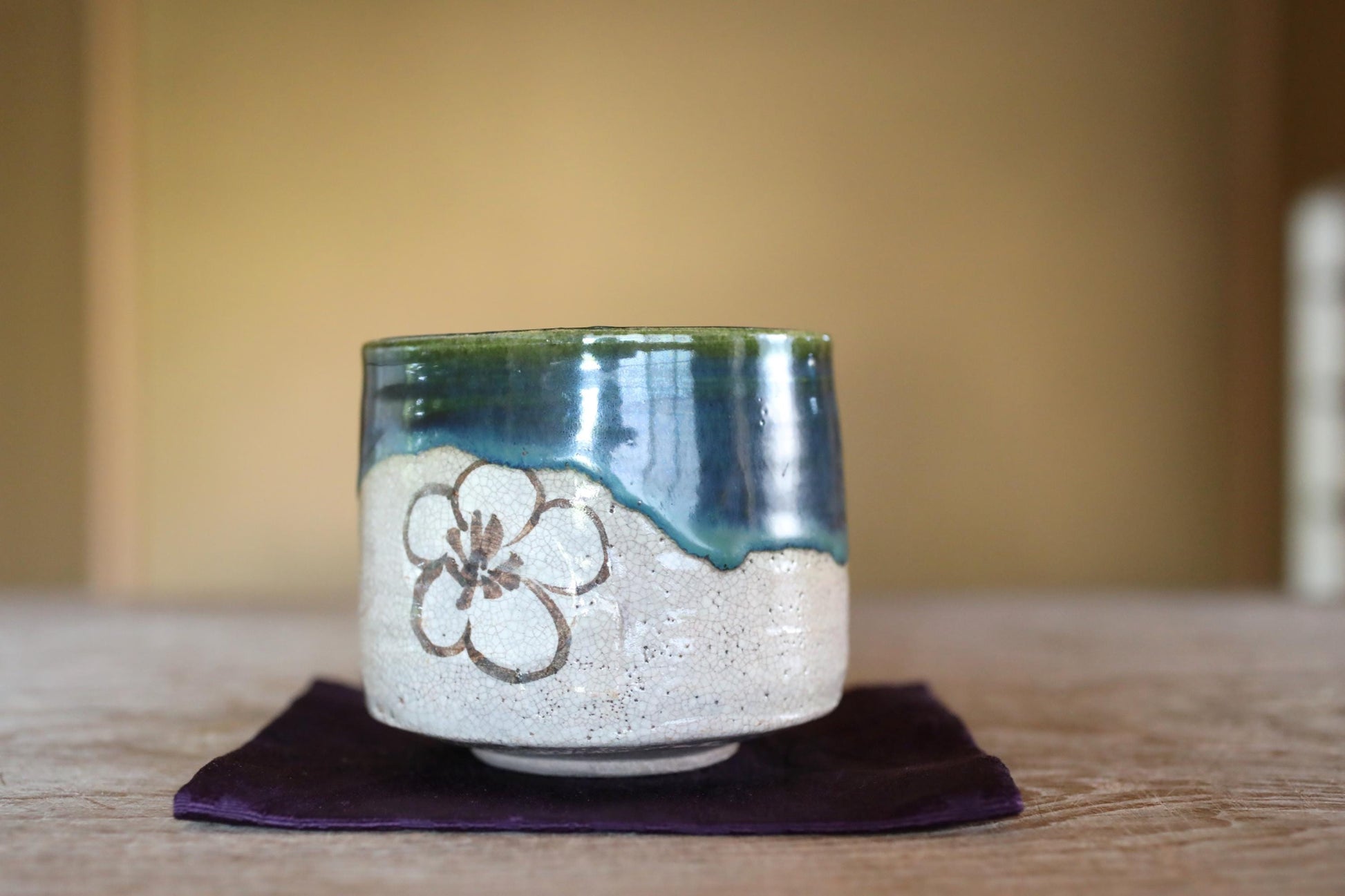A ceramic mug with a flower design sits on a purple cloth on a wooden surface.