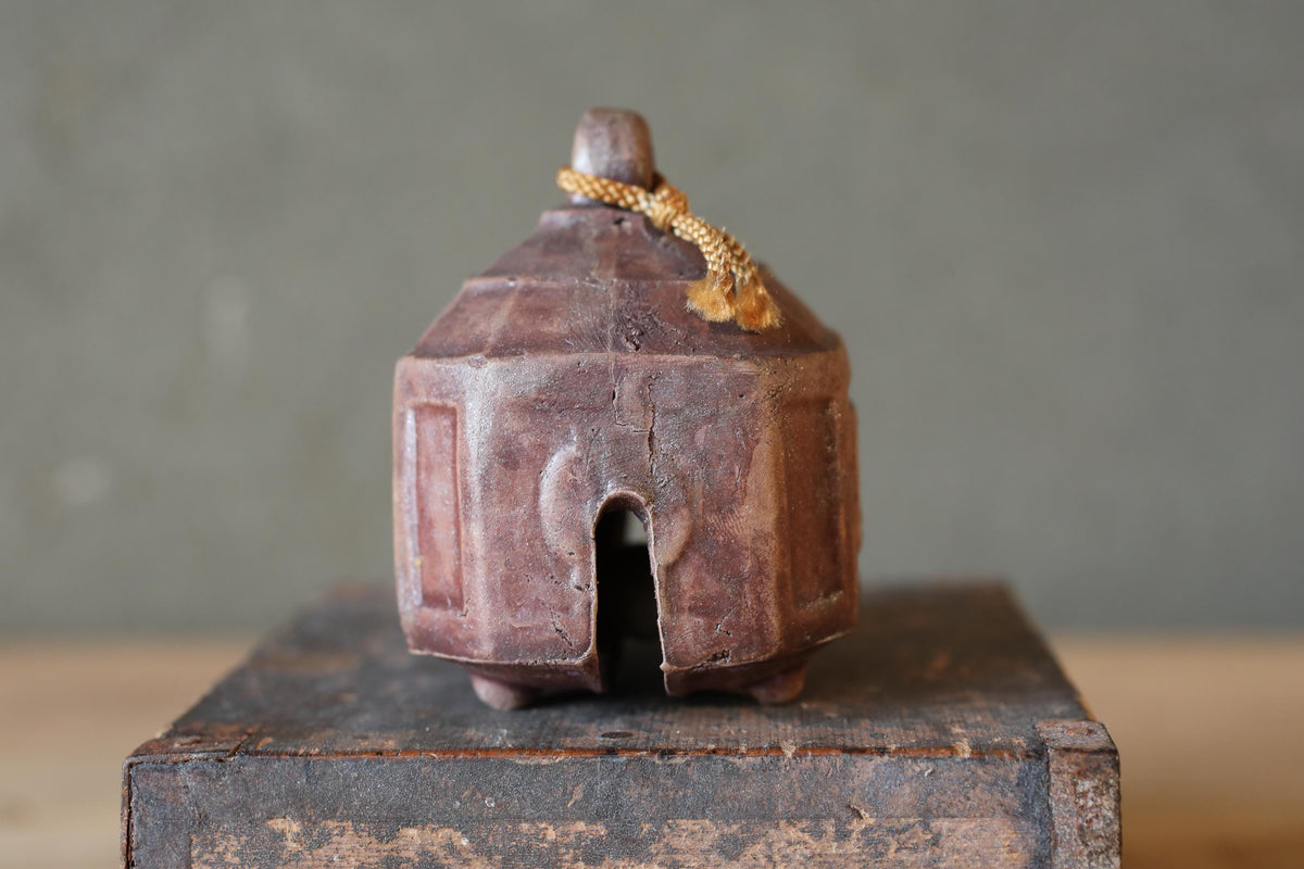 An old, rusted metal bell with a wooden base, sitting on a wooden surface against a gray background.