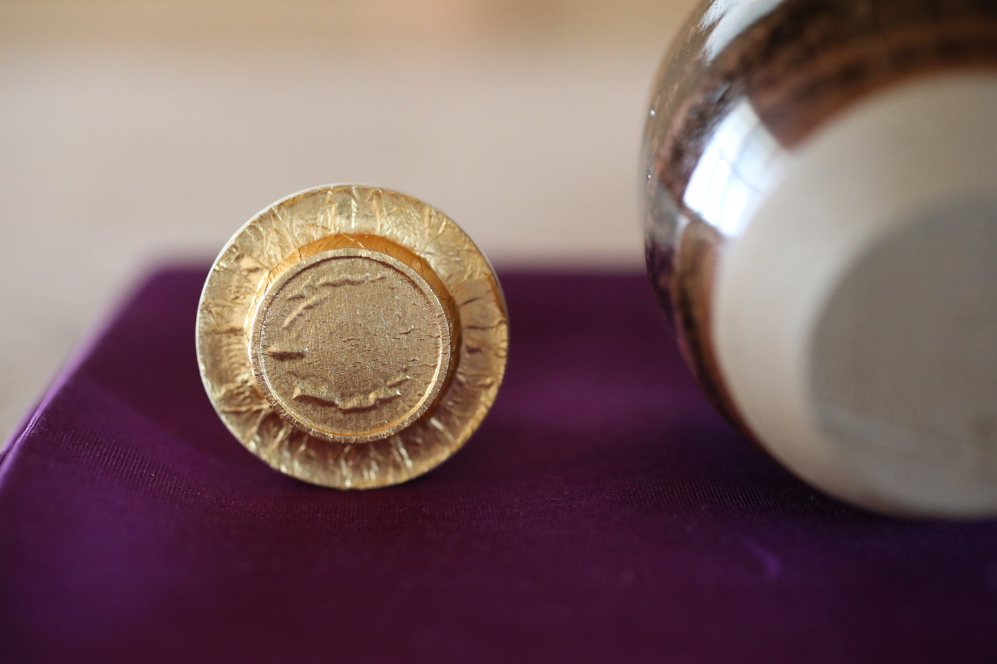 a close-up of a golden-colored object, possibly a small decorative piece, placed on a purple surface next to a larger, more ornate object.