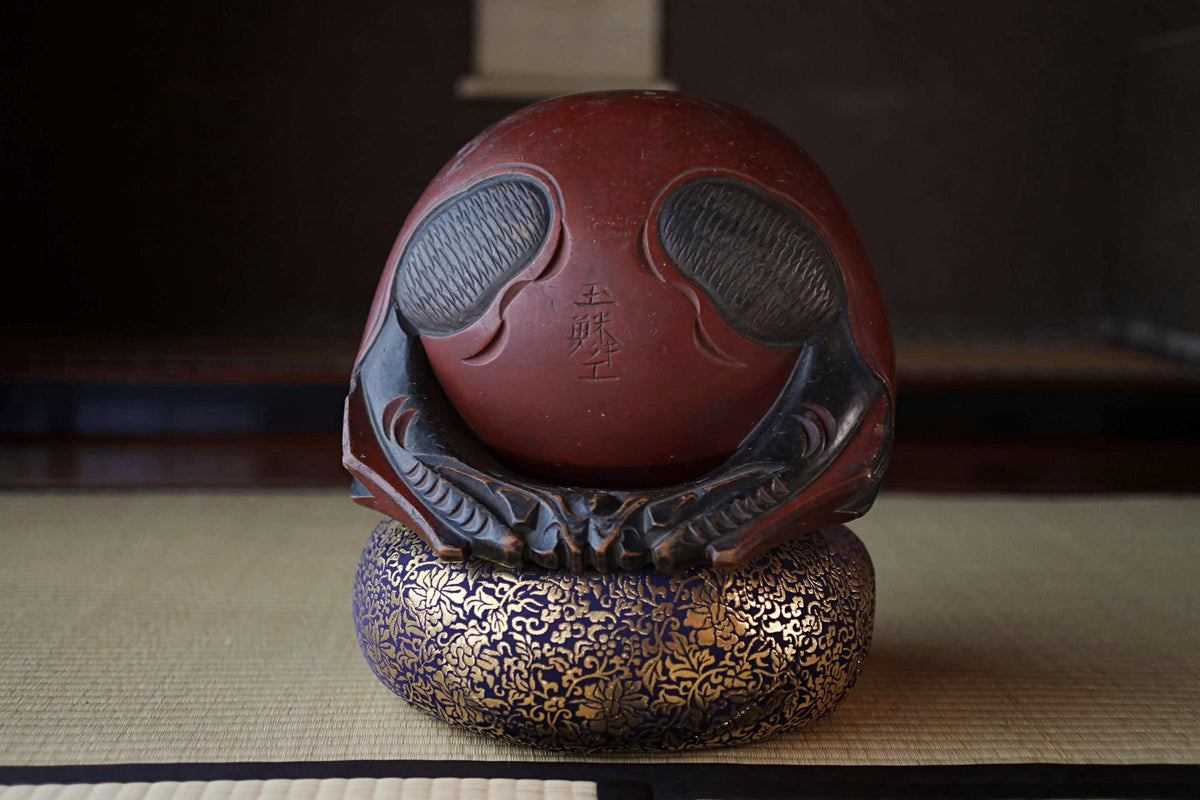 A red ceramic object with a carved face and text, sitting on a decorative blue and gold base.
