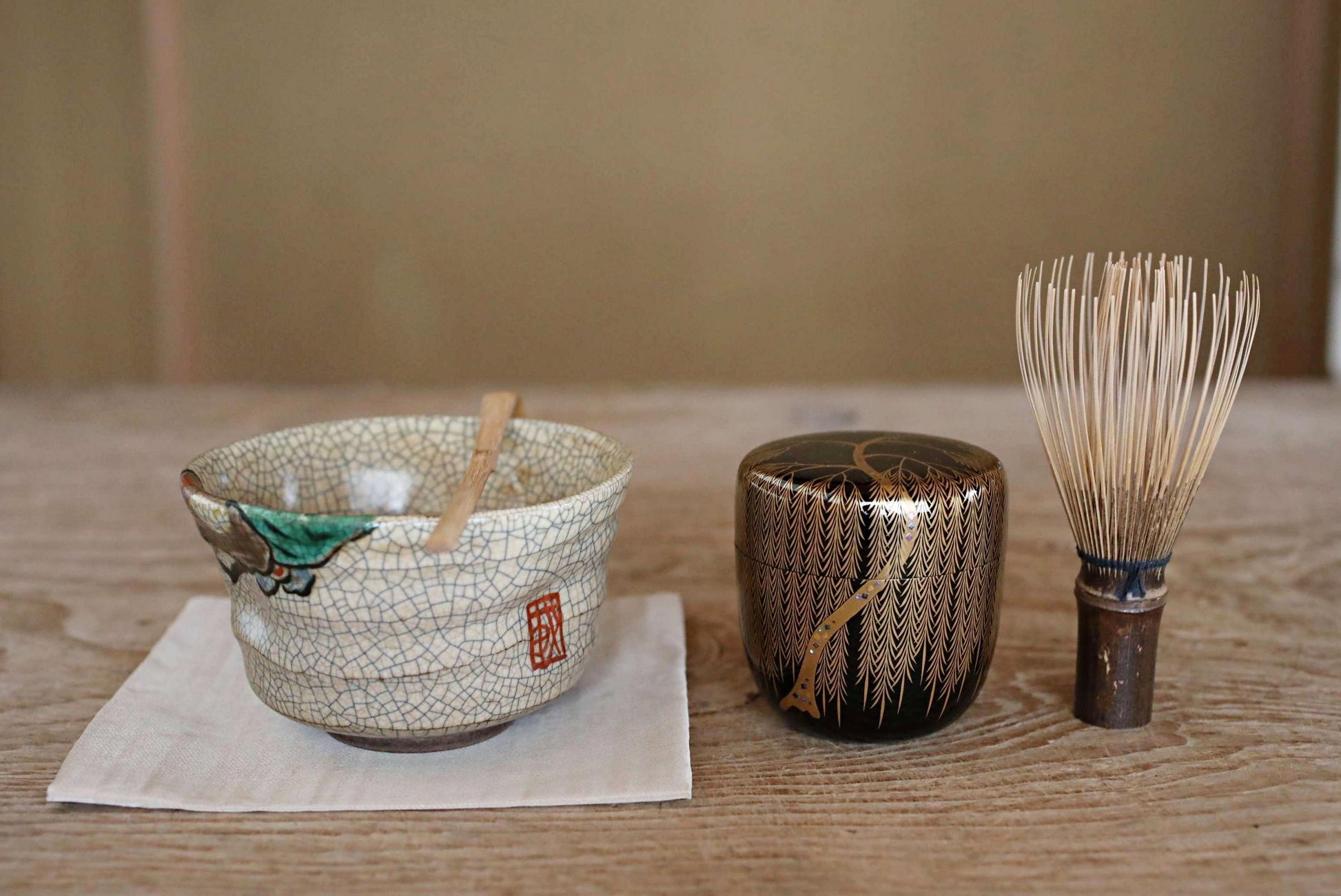 a variety of Japanese tea-making utensils and containers, including a bowl with a green design, a small black container, and a whisk.