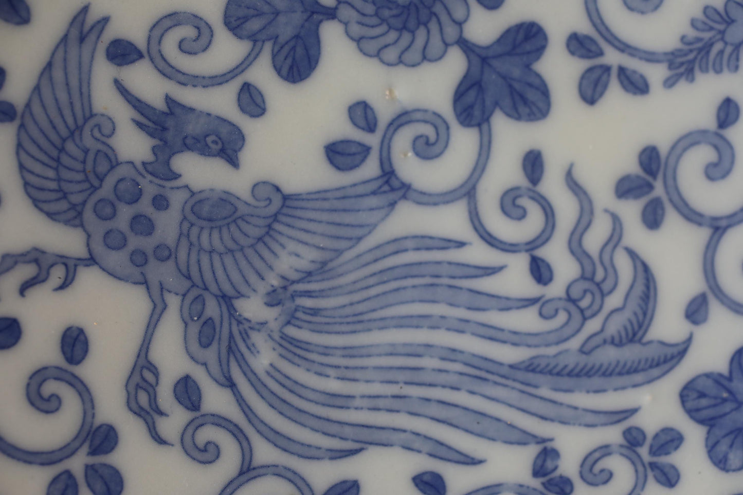 a close-up view of a decorative blue and white pattern, possibly a floral design or a bird-like figure. The pattern is intricate and detailed, with various elements such as leaves, flowers, and swirls creating a visually appealing and harmonious composition.