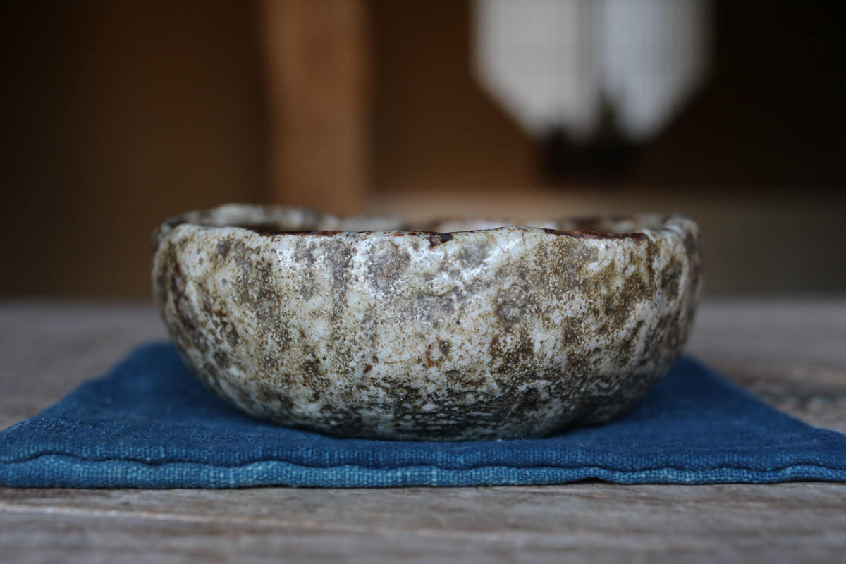 A close-up image of a ceramic bowl with a textured surface, placed on a blue cloth on a wooden surface.