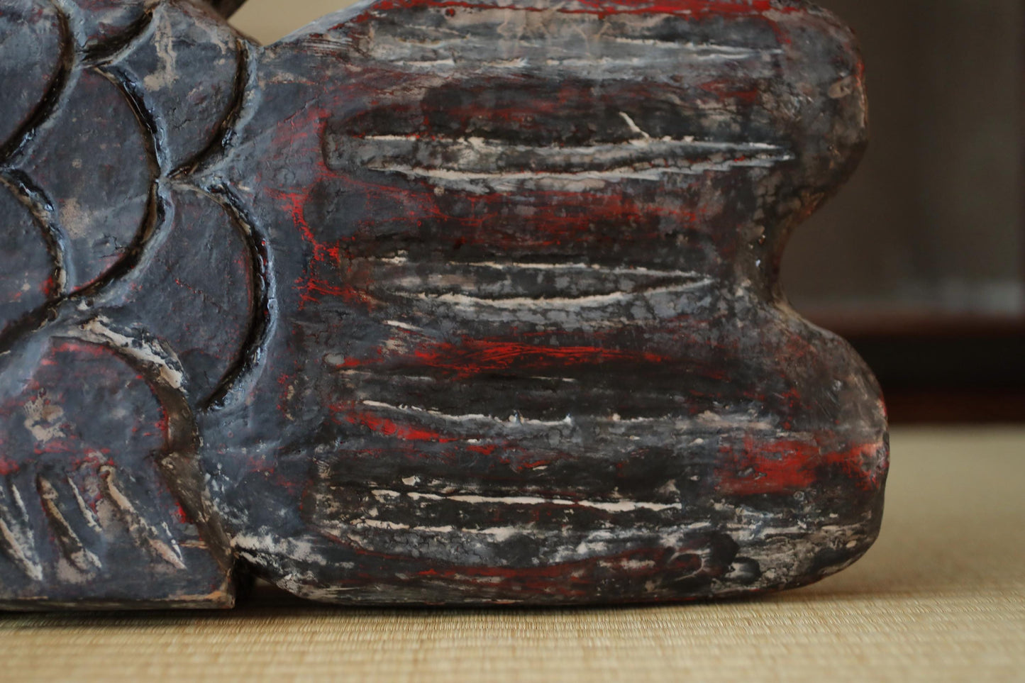 a close-up view of a dark, textured surface with red and black stripes or lines. The surface appears to be a wooden or stone object, possibly a sculpture or a piece of furniture.