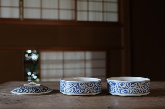 Three blue and white patterned bowls are arranged on a wooden surface, with a window and wooden frame in the background.