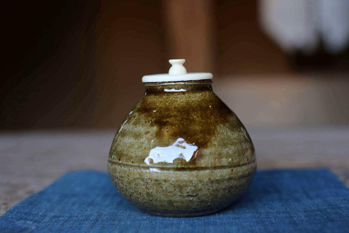 A brown ceramic jar with a white lid sits on a blue cloth.