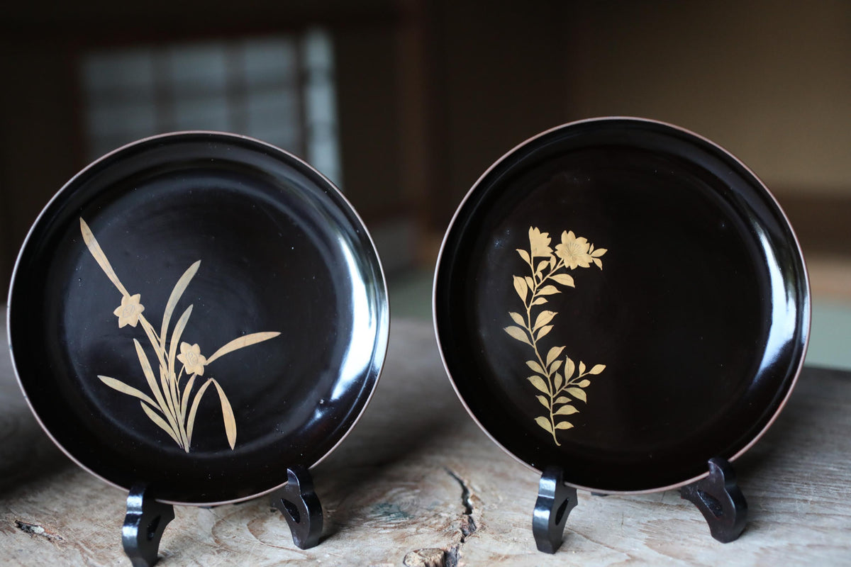 two black plates with gold floral designs, placed on a wooden surface.