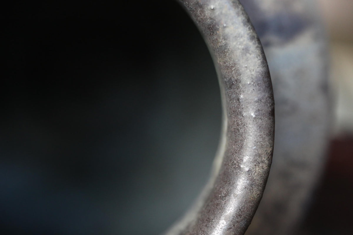 A close-up view of a metal object, possibly a pipe or tube, with a blurred background.