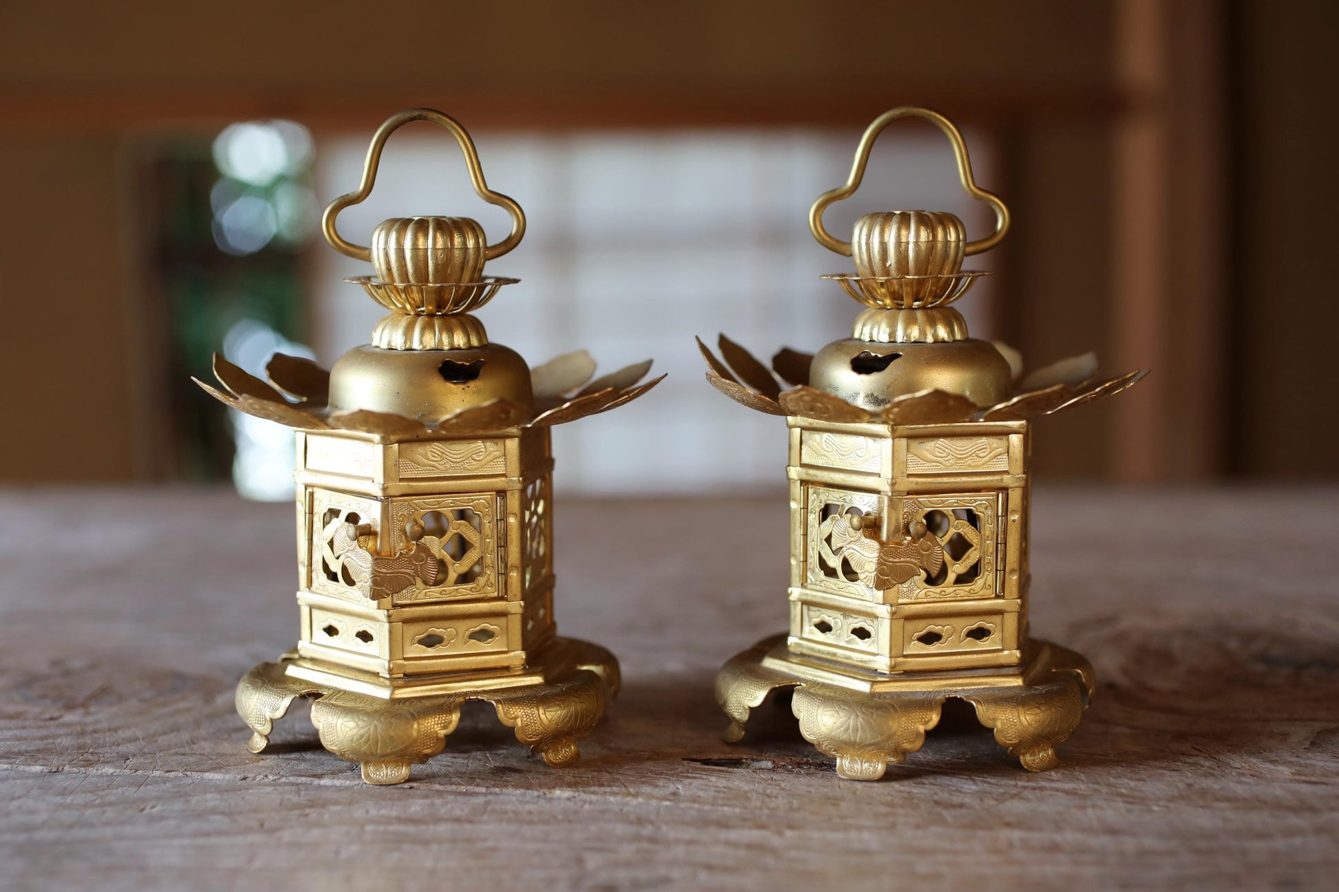 Two ornate golden lanterns with intricate designs are displayed on a wooden surface.