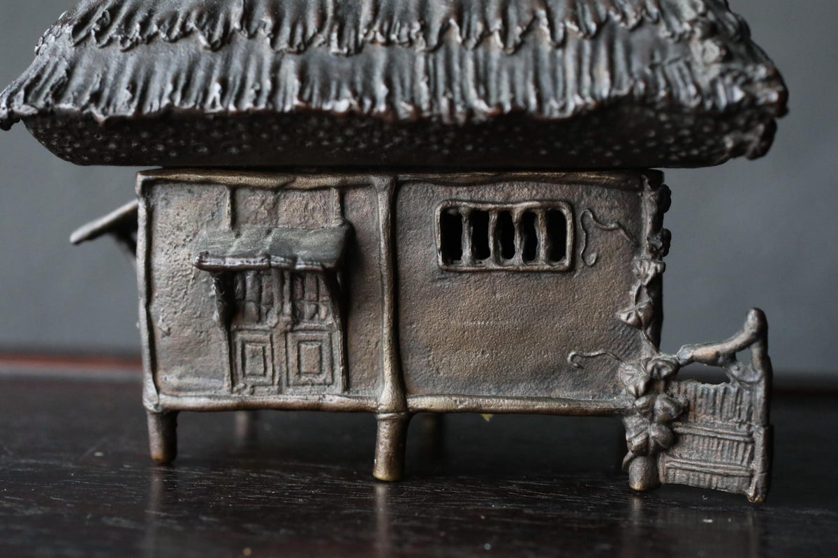 A small, intricately designed metal figurine depicting a traditional Chinese house with a thatched roof.