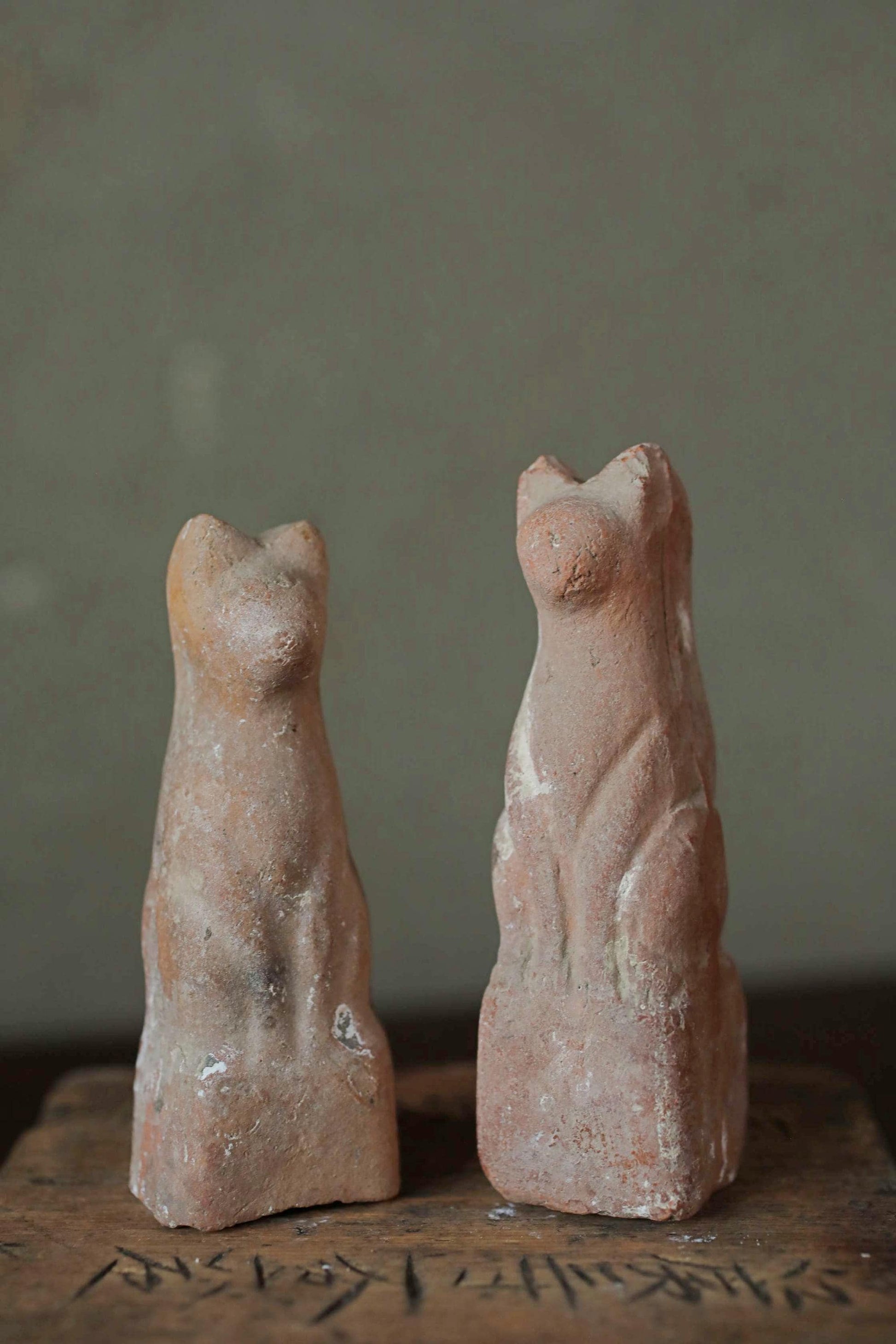 Two ancient clay cat statues stand side by side against a gray background.