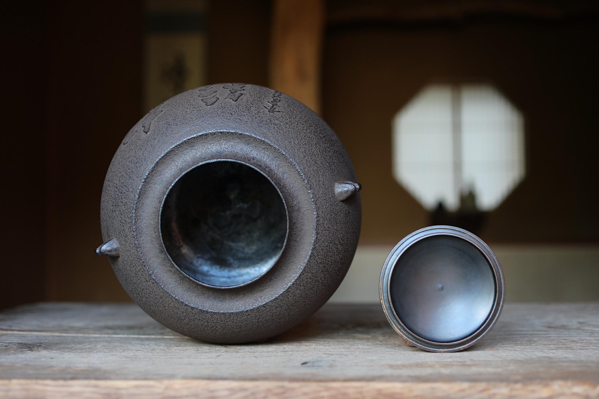 A black ceramic tea pot with a round opening sits on a wooden surface, with a smaller lid placed next to it.