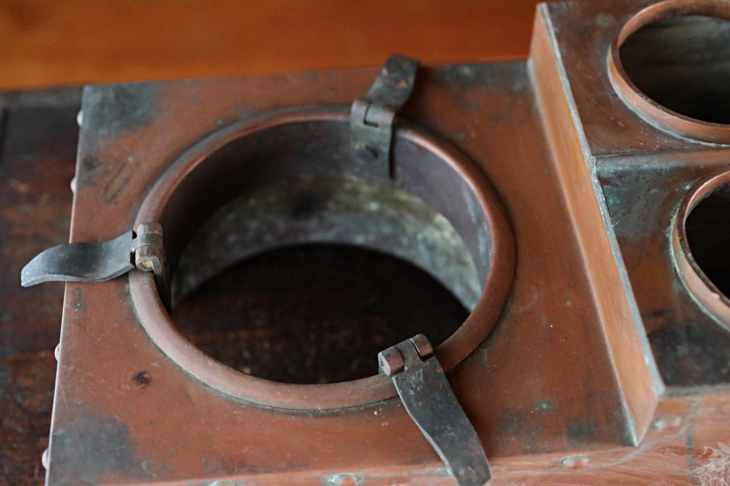 a close-up view of a metal container with a circular opening, featuring two metal clasps on the sides.