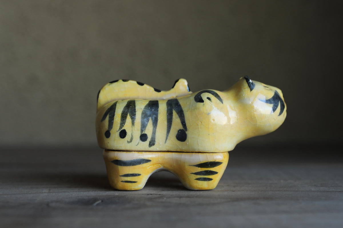 A ceramic figurine of a tiger, painted in yellow and black, is sitting on a wooden surface.