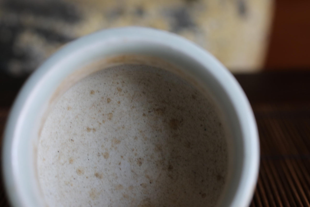A close-up view of a white ceramic mug with a creamy, frothy substance inside, possibly a beverage or a sauce.