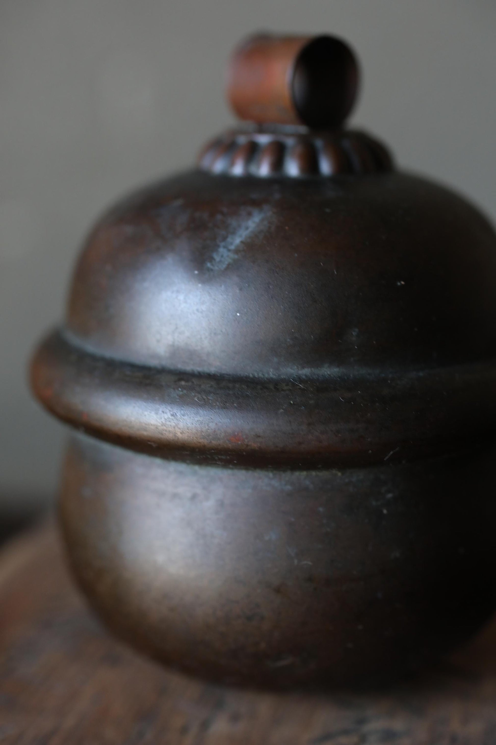 A close-up image of a dark, textured metal object, possibly a container or lamp shade, with a small, circular object on top.